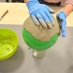 a person in blue gloves sanding on top of a green ball and yellow bowl