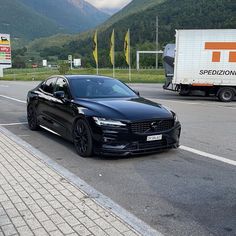 a black car is parked on the side of the road next to a white truck