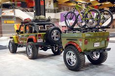 two green jeeps with bicycles on the back of them in a showroom area