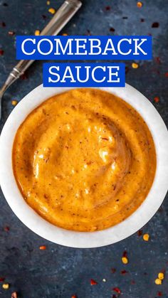 a white bowl filled with sauce next to a spoon on top of a blue surface