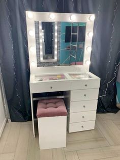 a white vanity with lights on it and a pink stool in front of the mirror