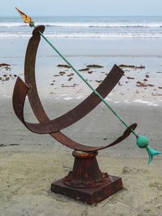 a metal sculpture on the beach with a green pole sticking out of it's center