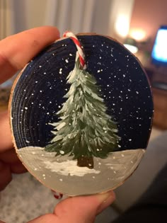 a hand holding a painted christmas ornament with a tree on it