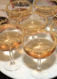 there are many wine glasses on the table with gold rims and glitter in them