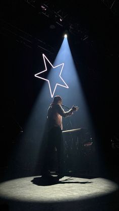 a man standing on top of a stage with a star above his head in the dark