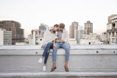 two women sitting on the edge of a building with their arms around each other as they hug