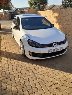 a white car parked on the side of a road next to a brick wall and fence