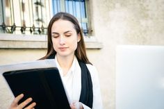 a woman is looking at something on her computer screen while holding an open book in front of her