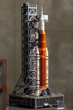 an orange and white model of a rocket on a wooden table next to a gray wall