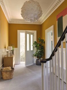 the hallway is painted yellow and has a basket on the bannister next to it