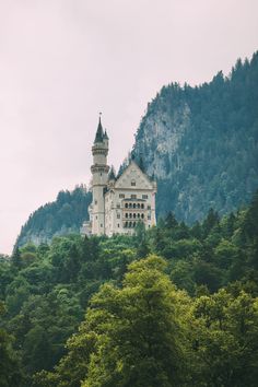 an old castle sits on top of a hill surrounded by green trees and tall mountains