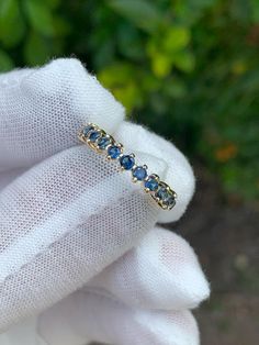 a gold ring with blue sapphire stones on it's side, in front of some bushes