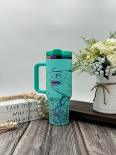 a blue coffee mug sitting on top of a wooden table next to a vase with flowers