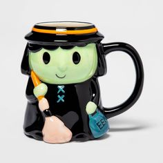 a black and green ceramic coffee mug with a small figure holding a blue handbag