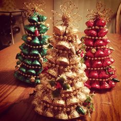 three christmas trees sitting on top of a wooden table next to each other with gold and red decorations