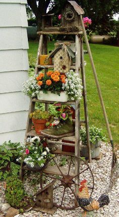 an old fashioned garden stand with flowers and chickens on it in front of a house