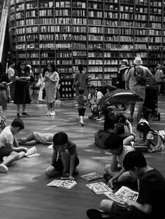 many children are sitting on the floor in front of bookshelves and looking at them