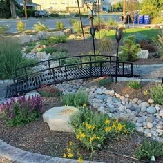 a garden with rocks and flowers in the foreground, along with a bridge that leads to a parking lot