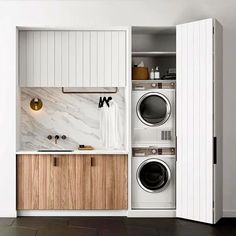 a washer and dryer in a small space with white walls, wood cabinet doors, and black tile flooring