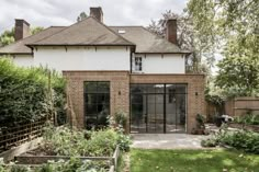 a brick house with glass doors and windows in the front yard, surrounded by greenery