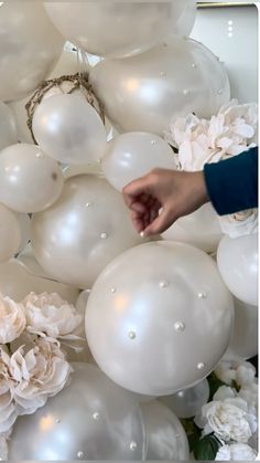 a bunch of white balloons with flowers on the bottom and one person reaching for them