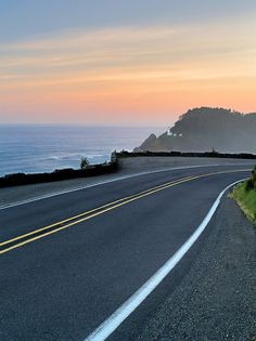 an empty road near the ocean at sunset