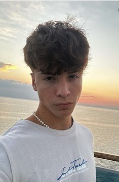 a young man standing in front of the ocean at sunset with his hair pulled back