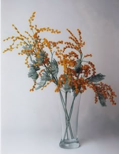 a glass vase filled with yellow flowers on top of a white table next to a wall