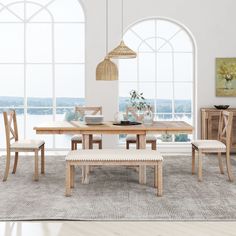 a dining table with four chairs and a bench in front of large windows overlooking the ocean