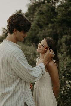 a man and woman standing next to each other talking on their cell phones in front of trees