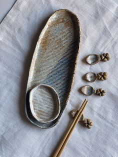 two chopsticks and an oval dish on a white tablecloth next to some shells