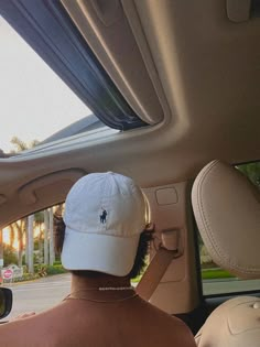 a man wearing a hat sitting in the driver's seat of a car looking out the window