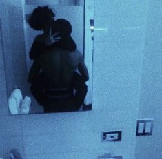 a man and woman are hugging in the bathroom mirror while looking at each other's reflection