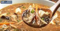 a wooden spoon full of soup with mushrooms and carrots on the side, in a white bowl