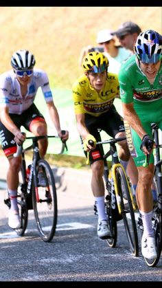 three men riding bikes on a road with people watching from the sidelines behind them