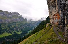 a house on the side of a cliff with mountains in the background