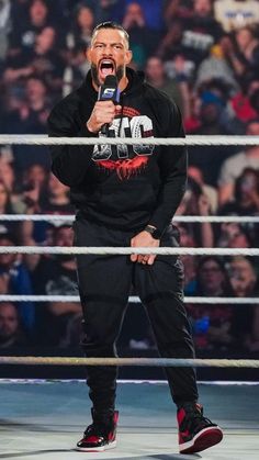 a man holding a microphone while standing in front of a crowd at a wrestling match