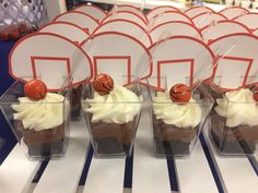 cupcakes with white frosting and red decorations in plastic cups on a table