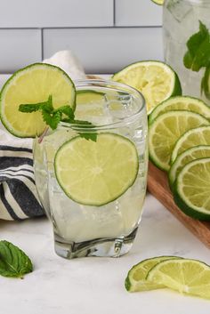 two glasses filled with lemonade and limes next to slices of lime on a cutting board