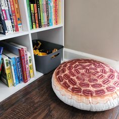 a pizza shaped pillow sitting on top of a wooden floor next to bookshelves