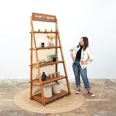 a woman standing next to a shelf with pots and plants on it in front of a white wall