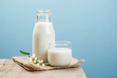 two glasses and a bottle of milk on a burlap cloth with a blue wall in the background