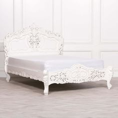 a white bed with ornate carvings on the headboard and foot board, against a white wall