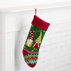 a green and red christmas stocking hanging from a mantel with white brick fireplace