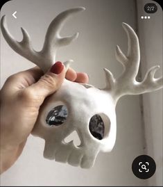 a hand holding a white skull with antlers on it's head and eyes