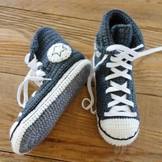 two crocheted sneakers with white laces are on a wooden floor, one is blue and the other is gray