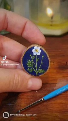 a hand holding a small blue flower in it's right hand next to a pen