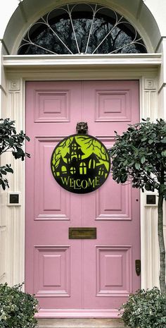 a pink front door with a welcome sign on it's side and potted trees