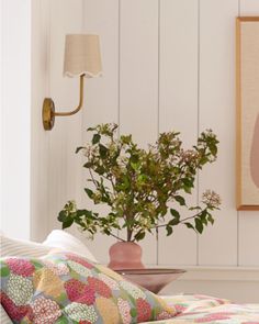 a plant in a vase sitting on top of a bed next to a wall light