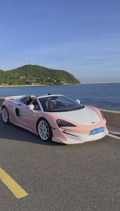 a pink and white sports car parked on the side of the road next to the ocean